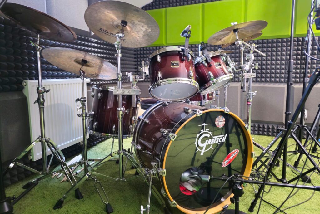 Perkusja Gretsch z talerzami i mikrofonami ustawiona na zielonym dywanie wśród paneli akustycznych
